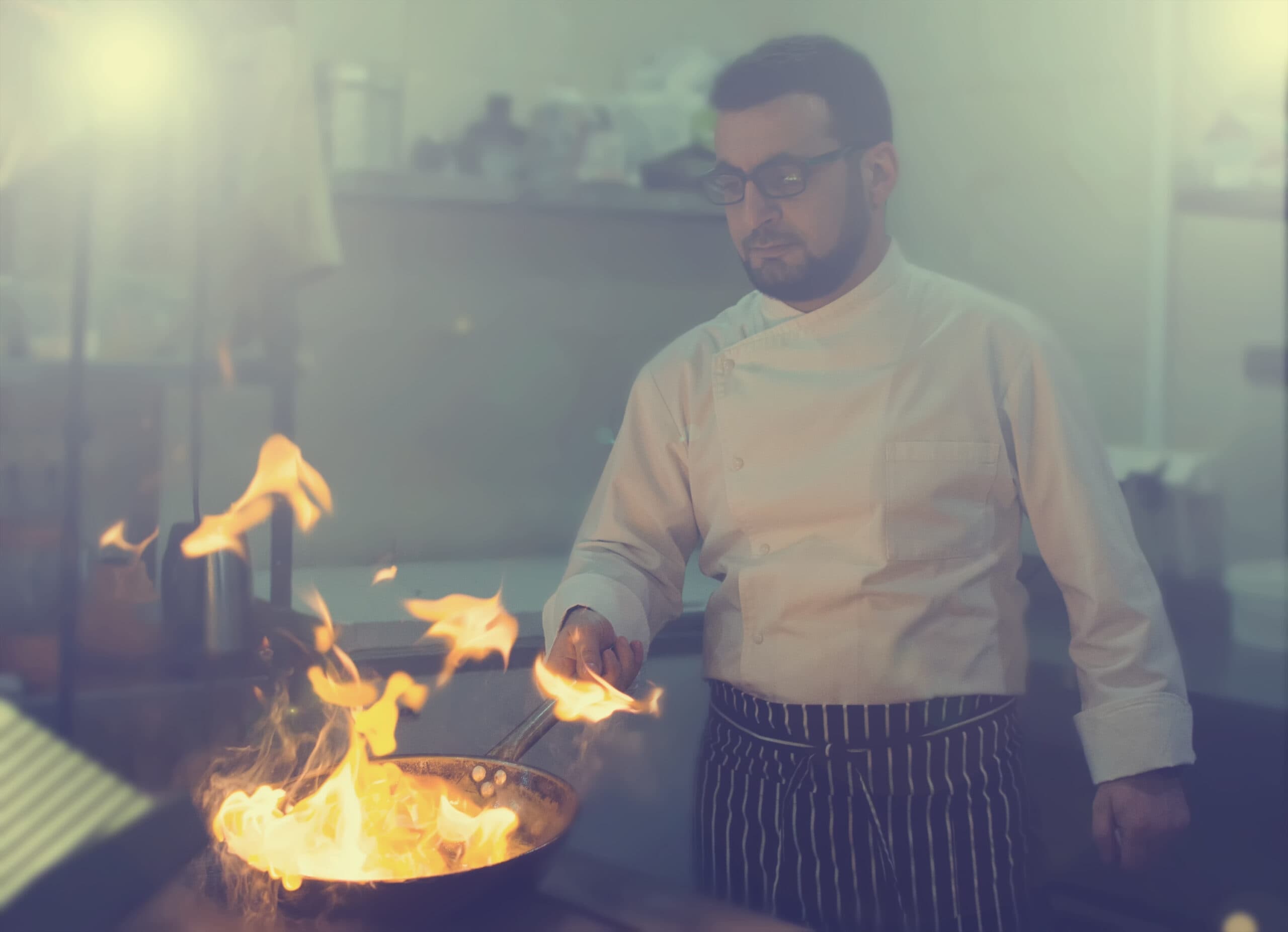 Chef flambéing beneath a commercial kitchen exhaust hood