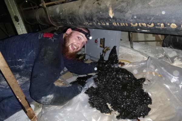 Proud hood cleaning technician displaying a thick layer of grease removed from a duct after diligent scraping