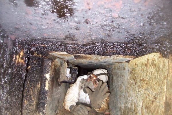 Technician carefully crawling through and cleaning a restaurant kitchen exhaust duct