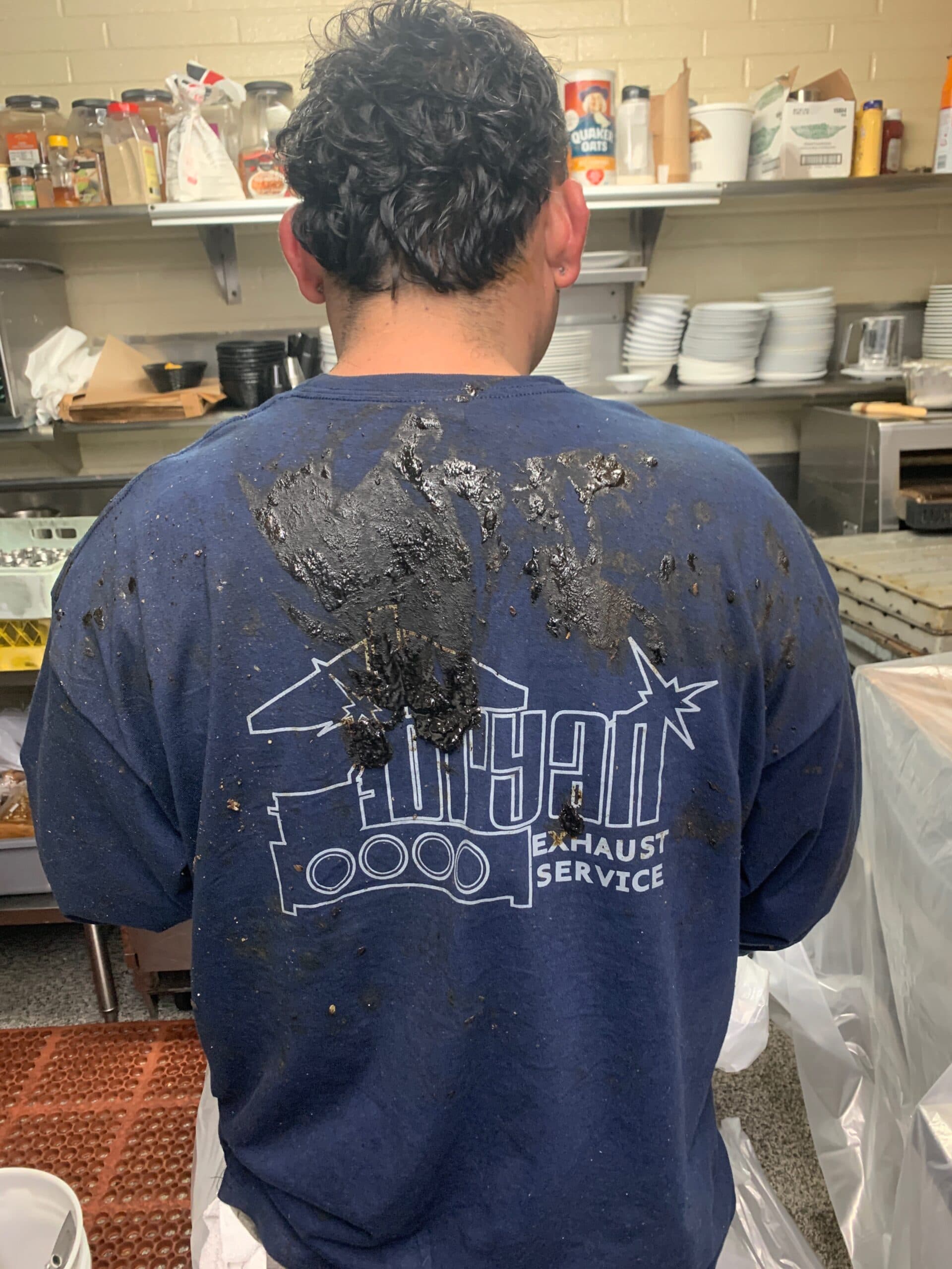 Bryan Exhaust technician in a grease-covered branded work shirt on the job in a commercial kitchen